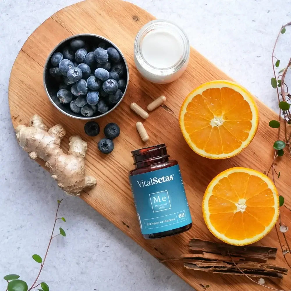 Cápsulas de Melena de León VitalSetas junto a frutas y jengibre en una tabla de madera.